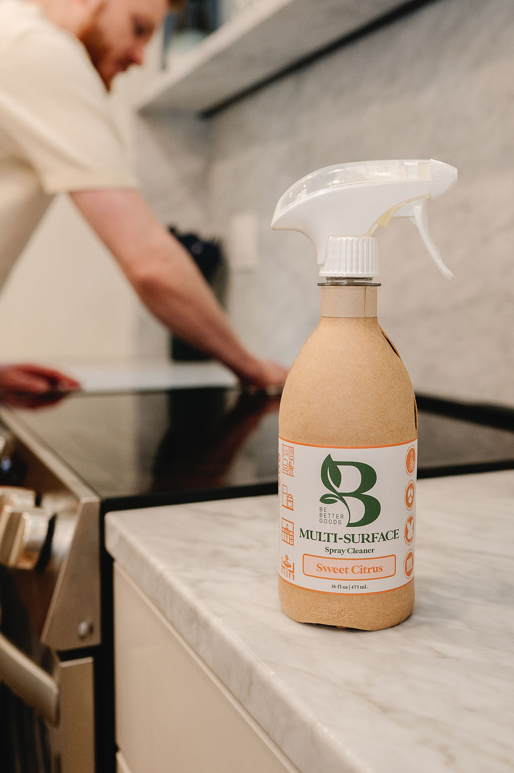 Multi-Surface Spray Cleaner in Sweet Citrus on a kitchen countertop in front of a stove being cleaned. 
